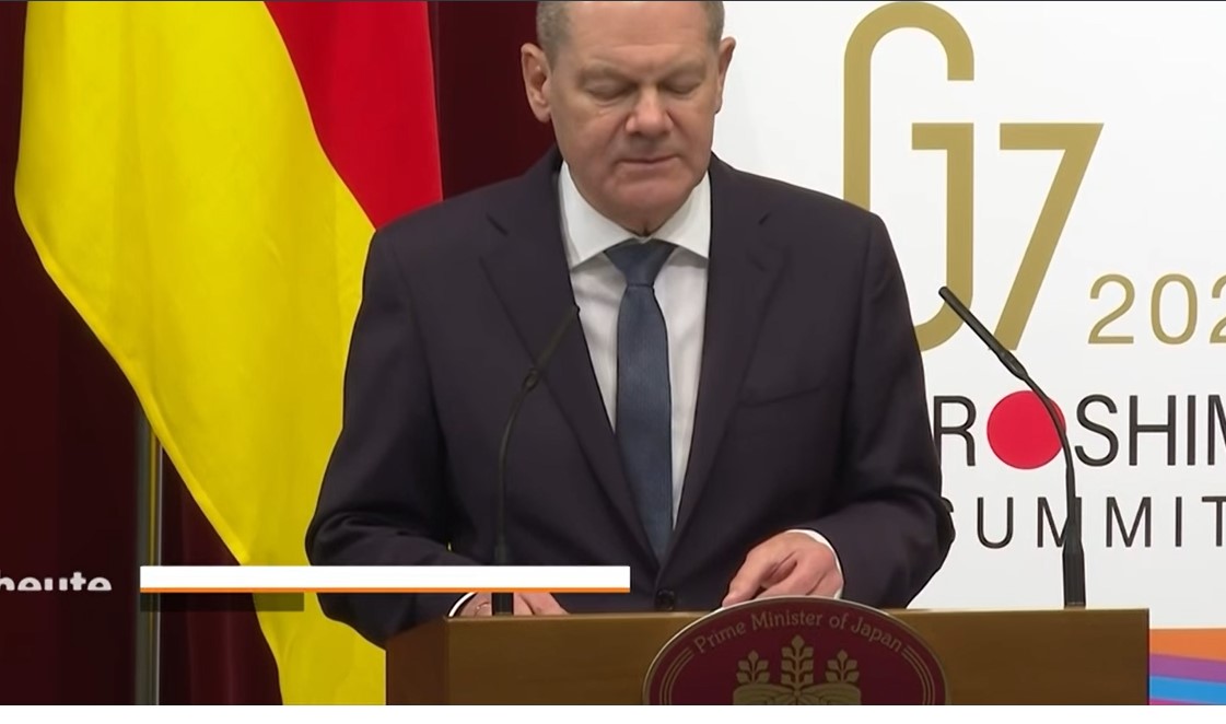 Bundeskaanzler Scholz ab Redepult mit Aufschrift, dass er jappanischer Präsident ist.